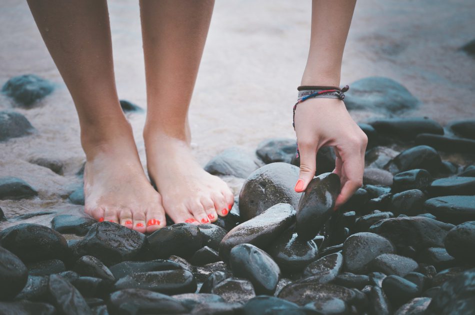 blote voeten met rode nagellak aan het strand meisje raapt steentje op